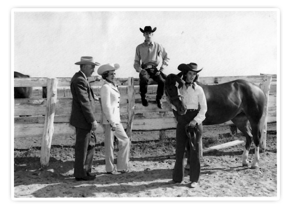 The Justin Family is posing on a fence, and daughter, Mary Justin, is holding the lead rope to a horse. 